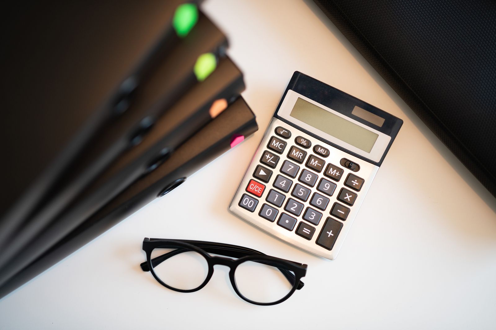 Calculator, binders, and eyeglasses on a desk.